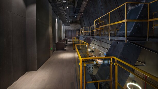Ein modernes Interieur mit einem langen Gang, gelben Geländern und einer Treppe mit Glasgeländern.