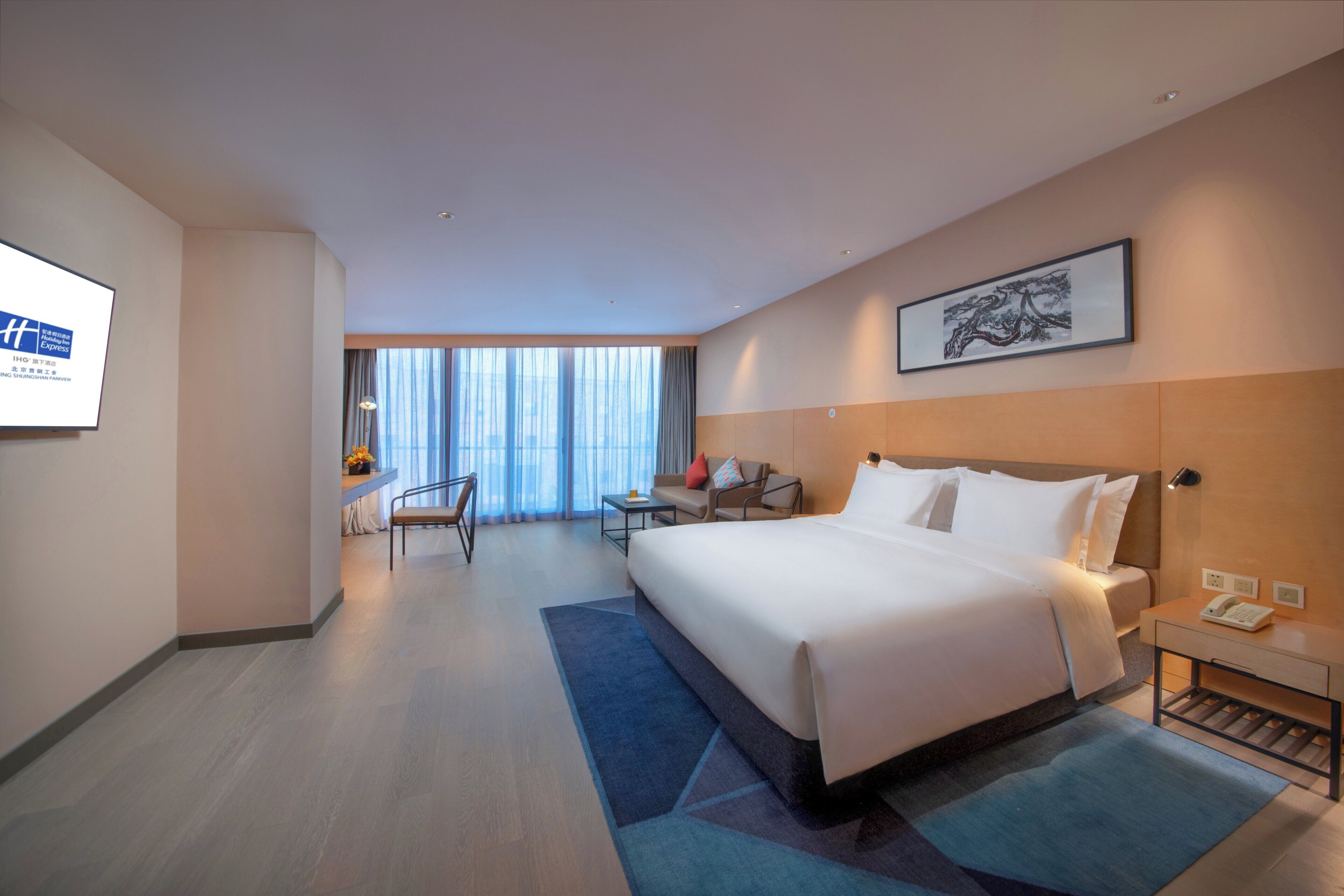 A hotel room with a large bed, a desk, a chair, and a view of the city through the window.