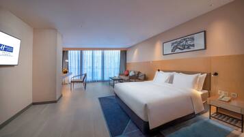 A hotel room with a large bed, a desk, a chair, and a view of the city through the window.