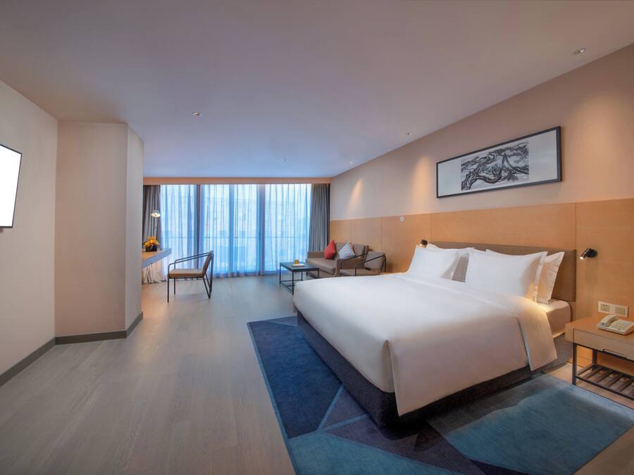 A hotel room with a large bed, a desk, a chair, and a view of the city through the window.