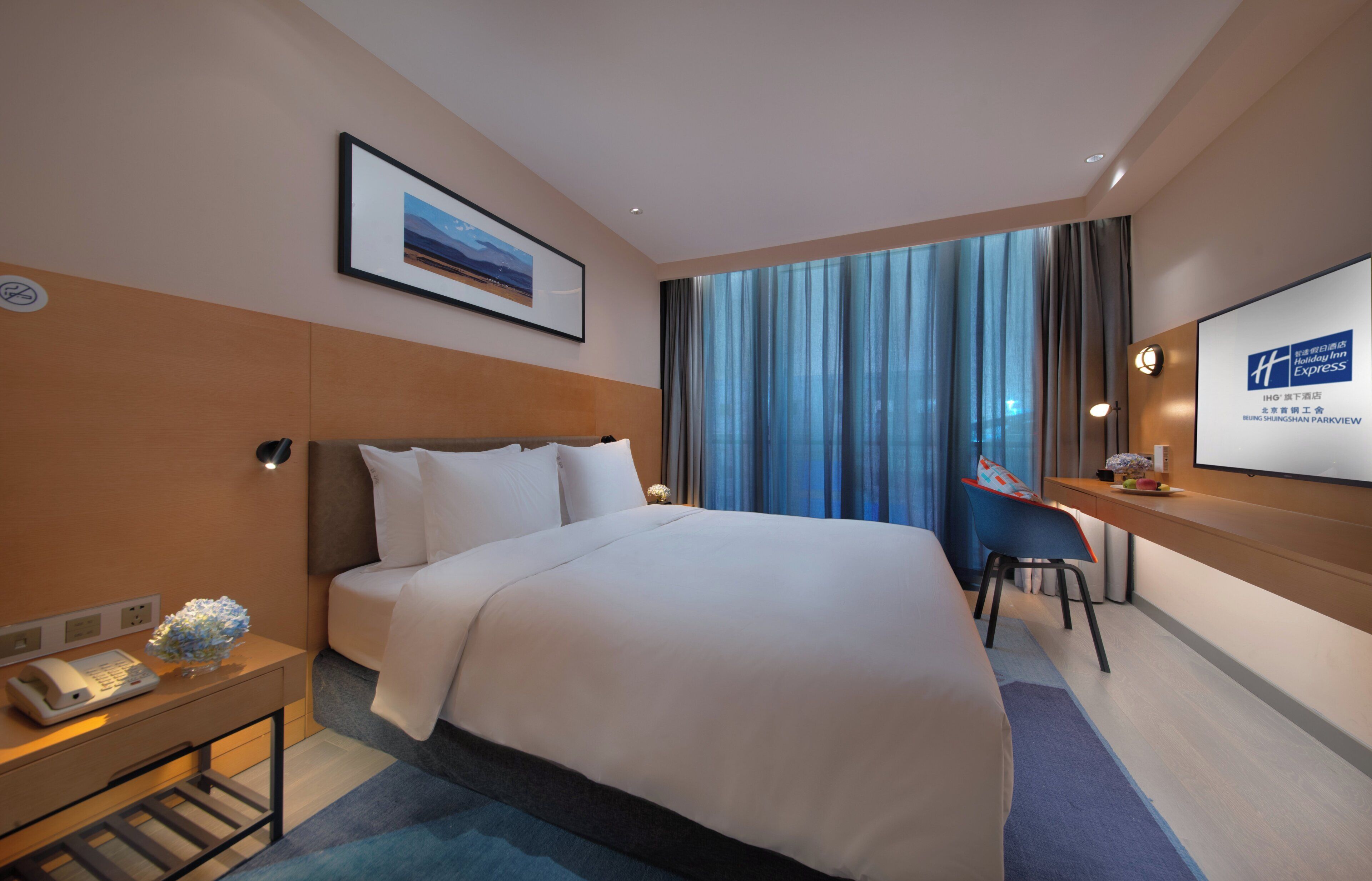 Habitación de hotel con cama, escritorio, silla, mesita de noche, teléfono y un cuadro en la pared.