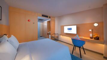 Ein Hotelzimmer mit einem großen Bett, einem Schreibtisch mit Computer und einem Fernseher an der Wand.