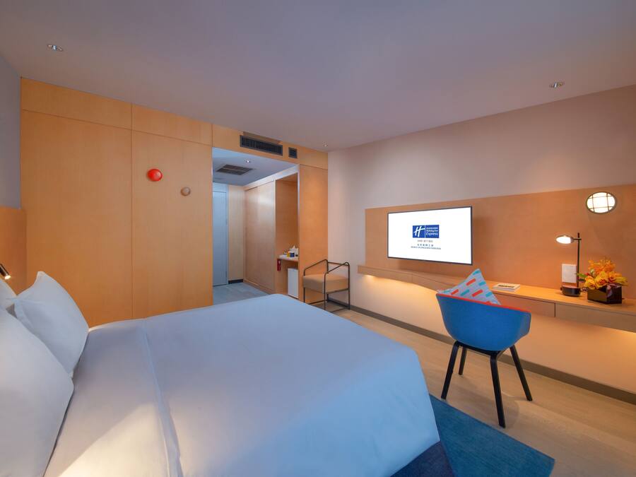 Et hotelværelse med en stor seng, et skrivebord med en computer og et fjernsyn på væggen.