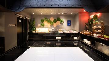 Un hall d’hôtel comprenant un comptoir d’accueil, une machine à café, un panneau indiquant « bonne cuisine et autres » et un mur végétal.