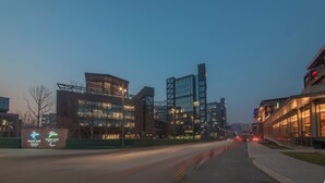 A modern building with a glass facade, a sign indicating an event, and a well-lit street. - Holiday Inn Express Beijing Shijingshan Parkview by IHG (Beijing)
