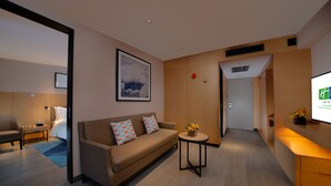 Ein modernes Hotelzimmer mit einer Couch, einem kleinen Tisch mit einer Vase, einem Fernseher und einem Bett im Hintergrund.