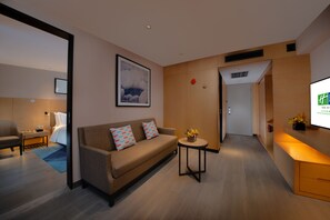 Quarto de hotel moderno com sofá, uma mesinha com um vaso, televisão e uma cama ao fundo.