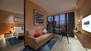 Ein modernes Hotelzimmer mit Bett, Sofa, Schreibtisch und einem großen Fenster mit Blick auf die Stadt.