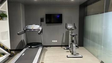 A gym with a treadmill, elliptical, and a TV on the wall.