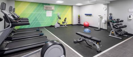Un gimnasio con cintas de correr, una elíptica, una banca, una pelota medicinal y mancuernas.