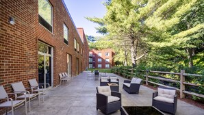 An outdoor patio with wicker furniture, a fire pit, and a view of a brick building and trees. - Holiday Inn Poughkeepsie by IHG (Poughkeepsie)