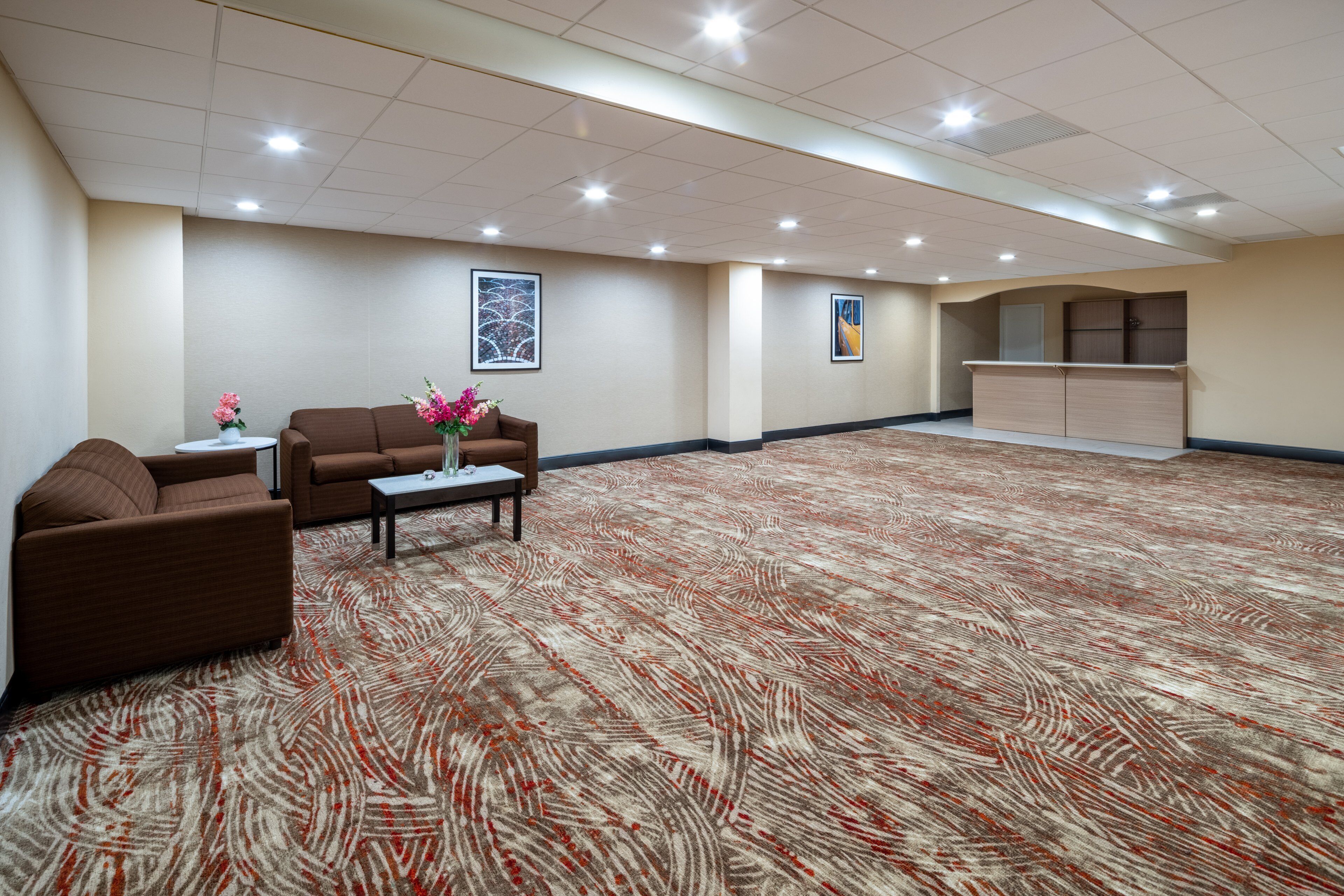 A spacious lobby with a patterned carpet, a brown sofa, a small table with a vase, and a reception desk.