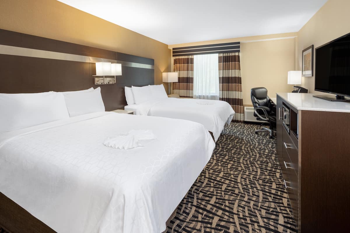 A hotel room with two beds, a desk, a chair, a television, and a window with curtains.