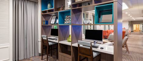 A modern office space with two desks, each with a computer and a chair, and a large shelving unit with various items.
