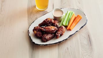A plate of chicken wings with celery and carrots, and a glass of yellow beverage on a wooden table.