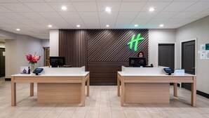 A reception area with two reception desks, a digital display, and a logo on the wall. - Holiday Inn Poughkeepsie by IHG (Poughkeepsie)