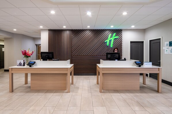 A reception area with two reception desks, a digital display, and a logo on the wall.