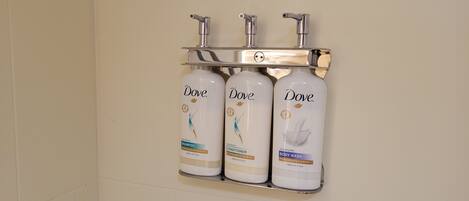 Une salle de bain équipée de trois produits Dove : un shampooing, un après-shampooing et un gel douche, le tout installé sur un distributeur mural.