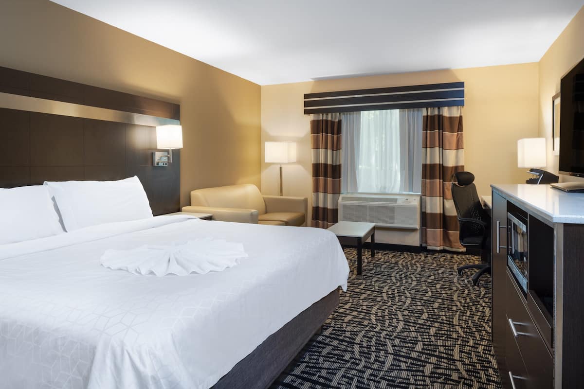 A hotel room with a large bed, a desk, a chair, a TV, and a window with curtains.