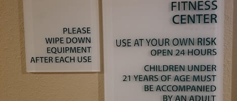Two signs on a wall. One sign says "Please wipe down equipment after each use." The other sign says "Fitness Center use at your own risk open 24 hours children under 21 years of age must be accompanied by an adult."