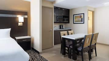 A hotel room with a bed, a desk, a chair, a microwave, and a painting on the wall.