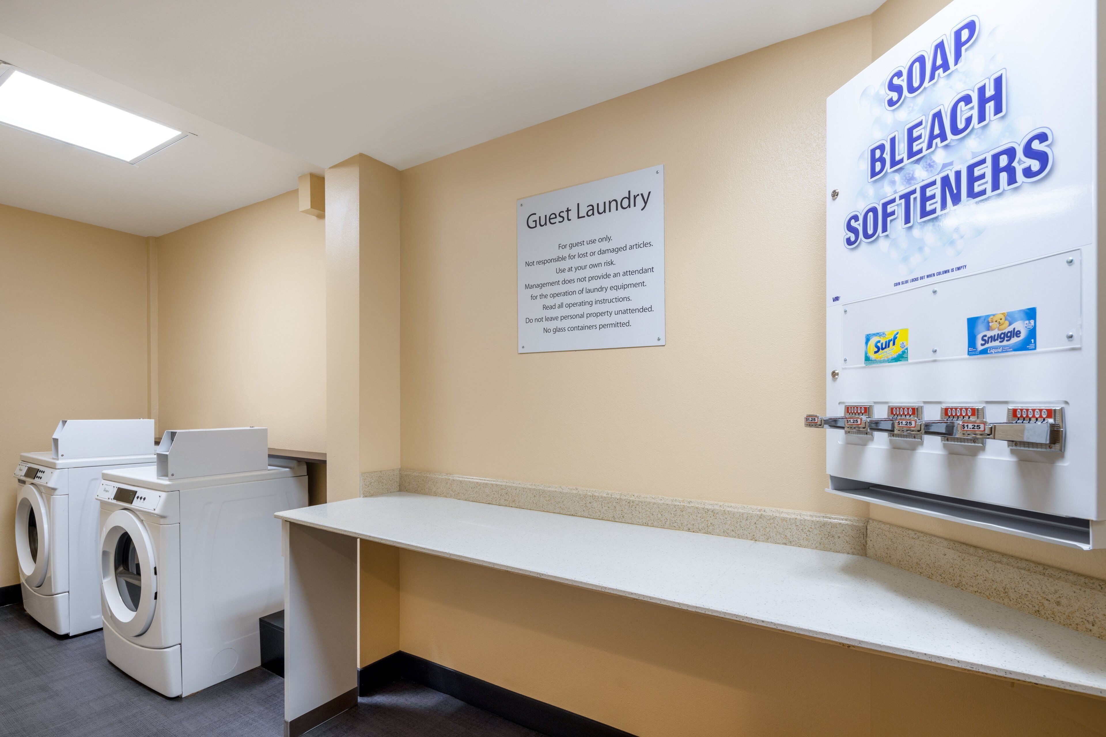 A guest laundry area with two washing machines, a sink, and a soap and bleach softener dispenser.