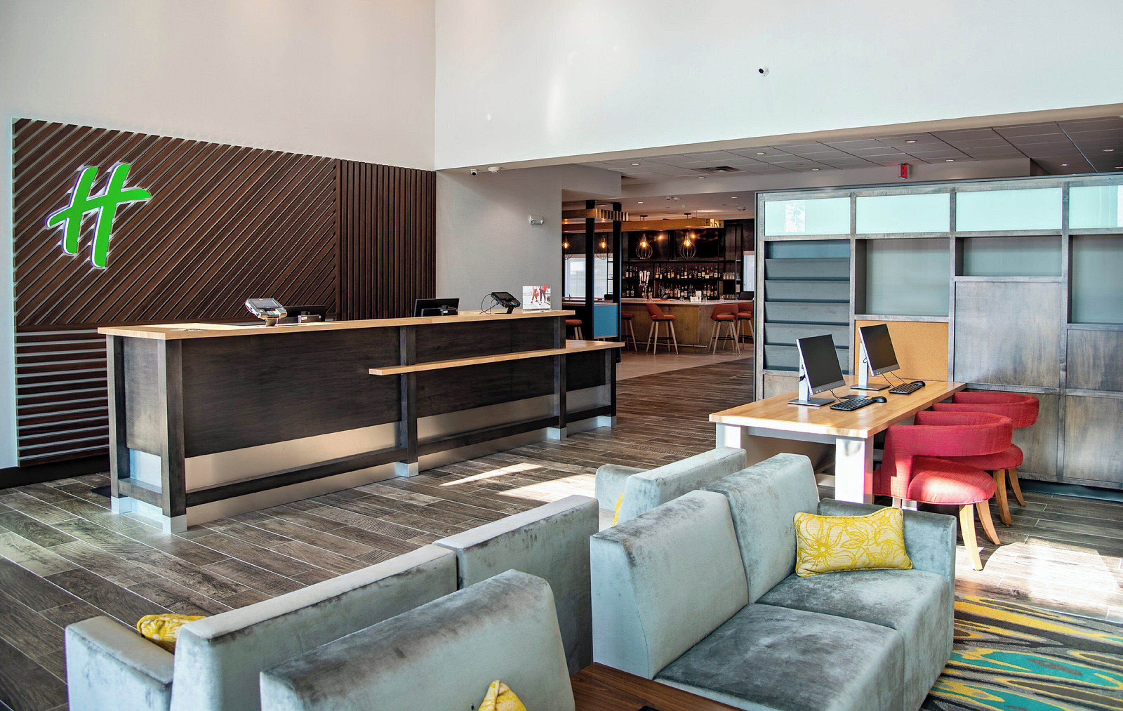 A modern hotel lobby with a reception desk, seating area, and bar.