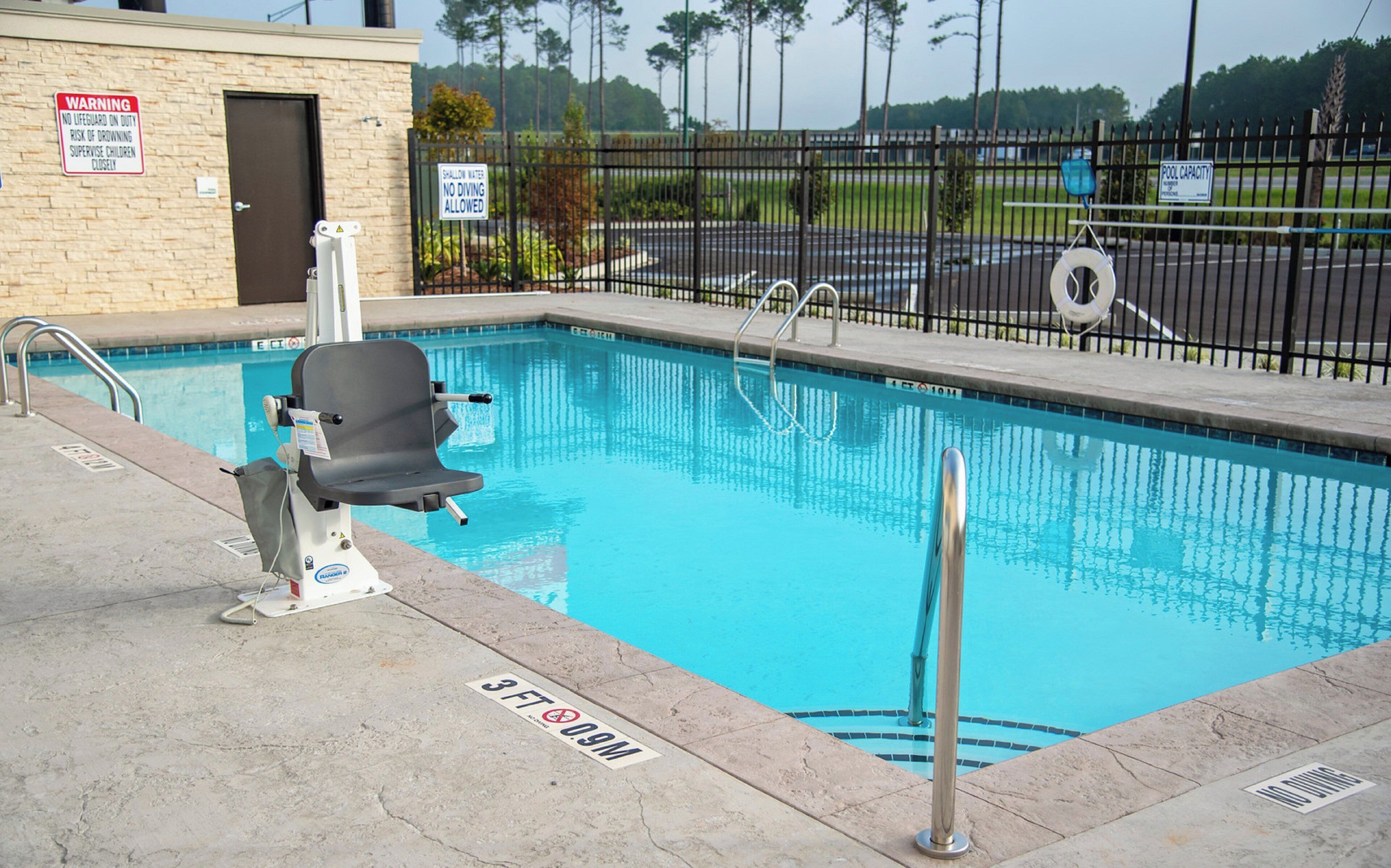 Une piscine équipée d’un poste de surveillance pour sauveteur, d’un panneau d’avertissement indiquant la faible profondeur de l’eau et d’un panneau indiquant la capacité maximale de la piscine.
