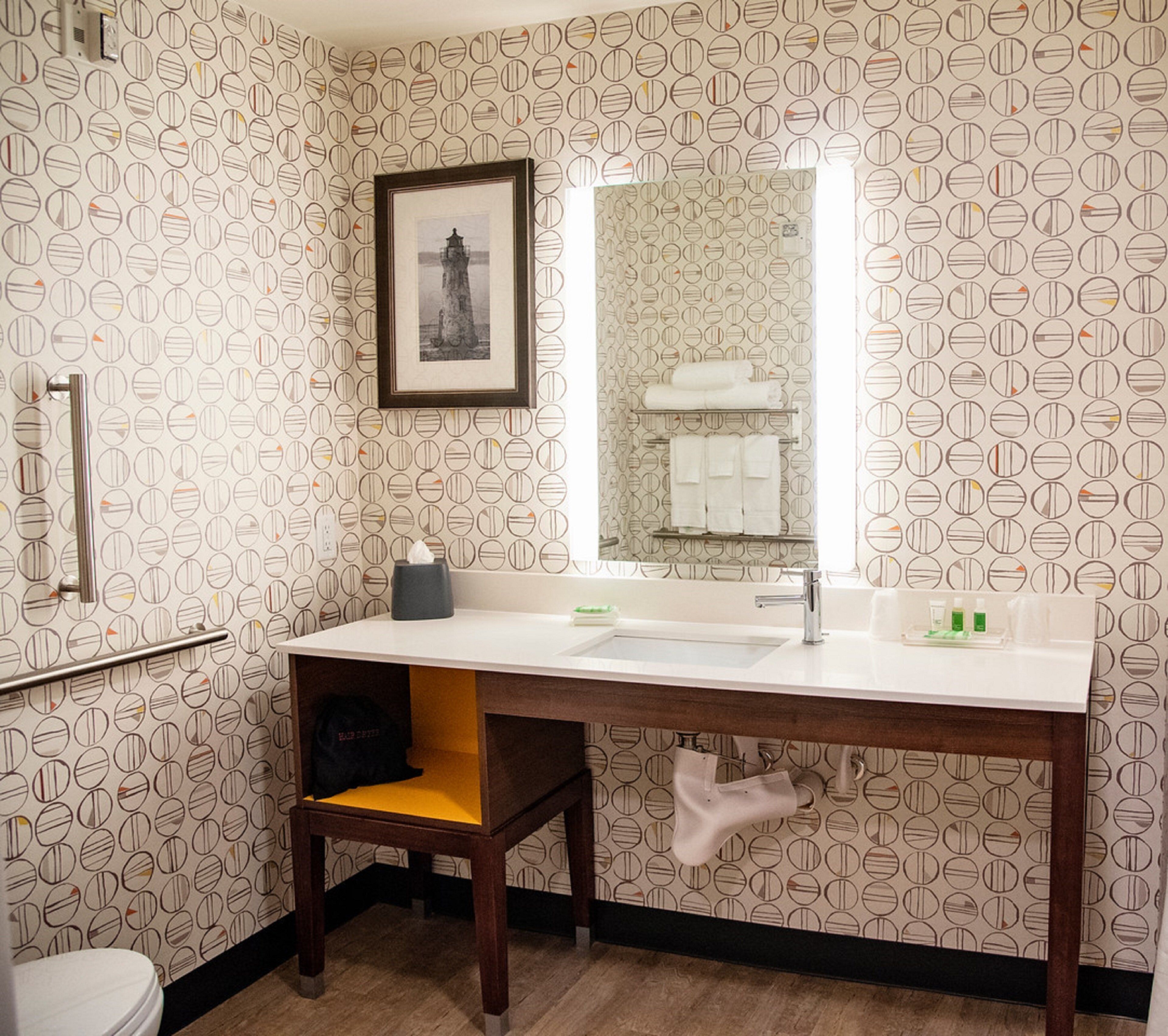 A bathroom with a round patterned wallpaper, a framed picture on the wall, a sink with a mirror, and a towel rack.