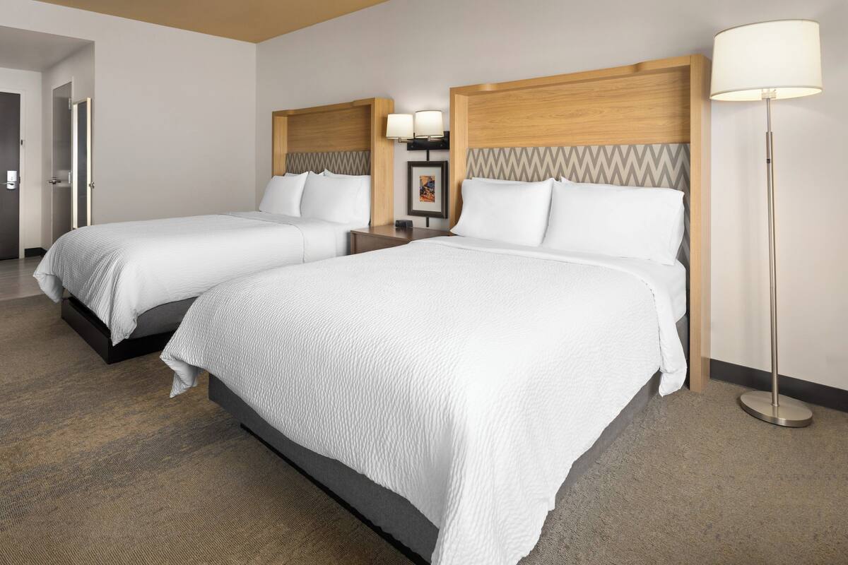 Ein Hotelzimmer mit zwei Betten, einem hölzernen Kopfteil, einer Stehlampe und einem Bild an der Wand.