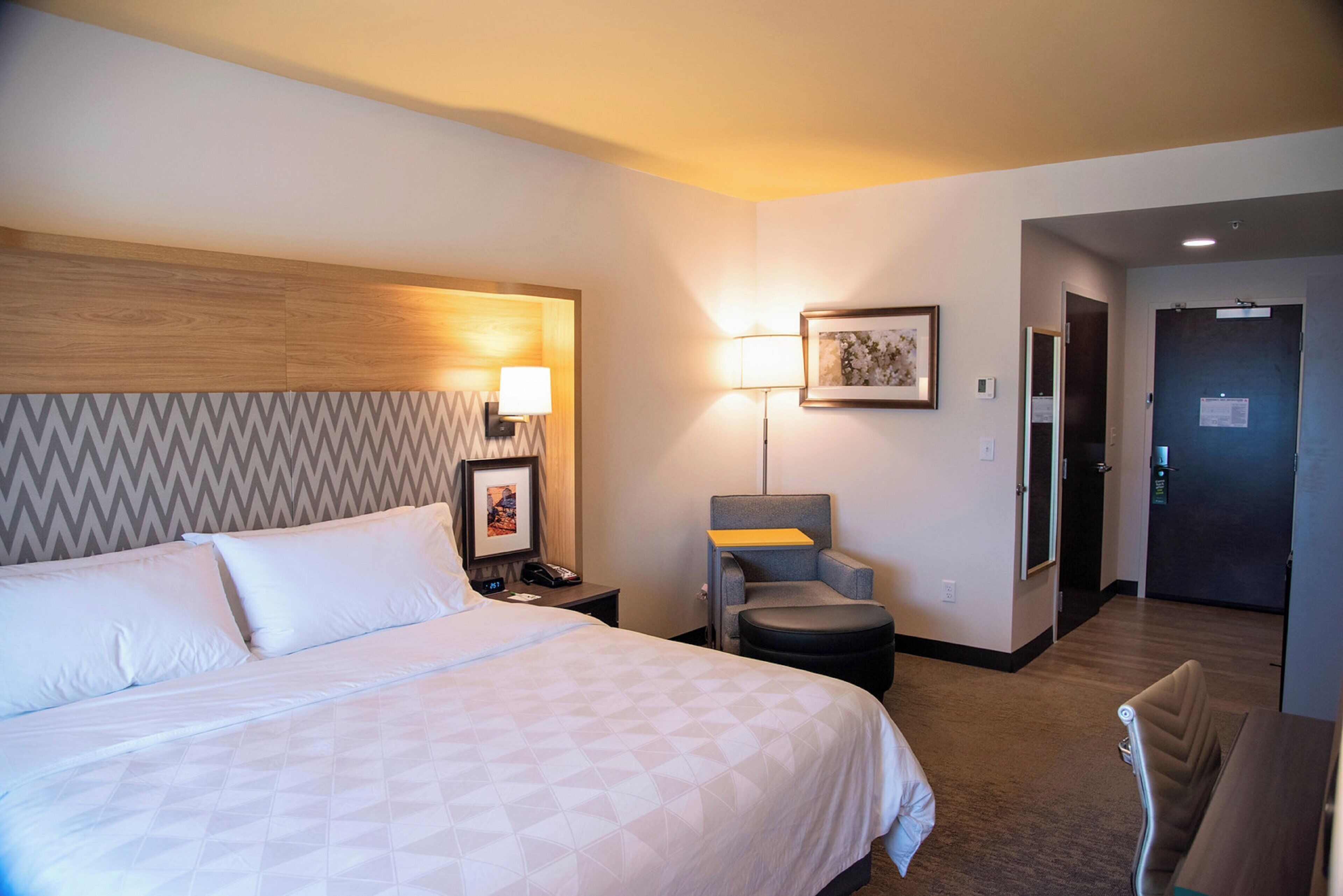 A hotel room with a bed, a chair, a desk, and a door.