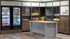 A corner kitchenette with a wooden countertop, a refrigerator stocked with beverages, and shelves with snacks and packaged goods. - Holiday Inn & Suites Savannah Airport - Pooler by IHG (Pooler)