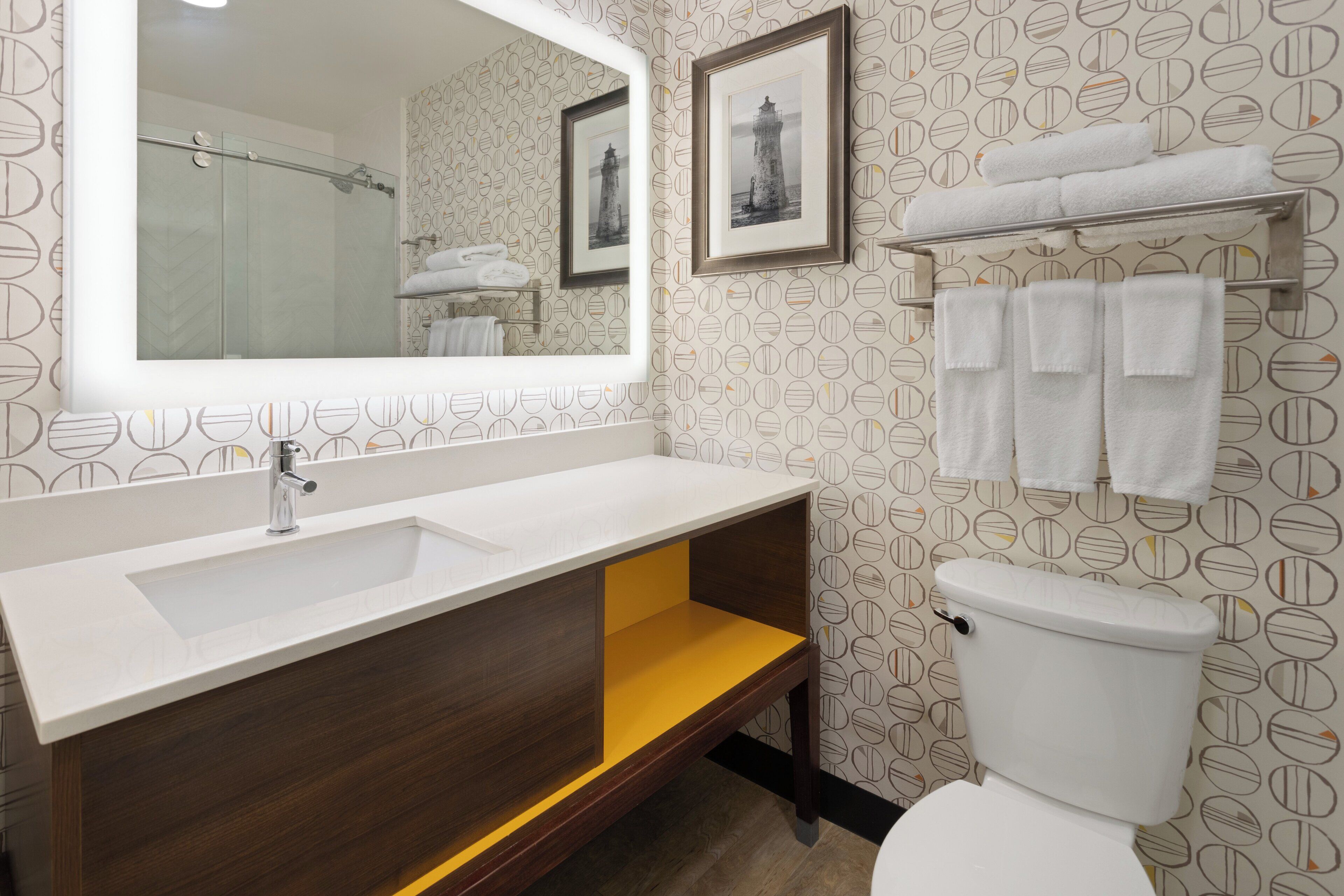 Une salle de bain avec un lavabo blanc, un miroir et des toilettes. Des serviettes sont suspendues sur un porte-serviettes placé au-dessus des toilettes.