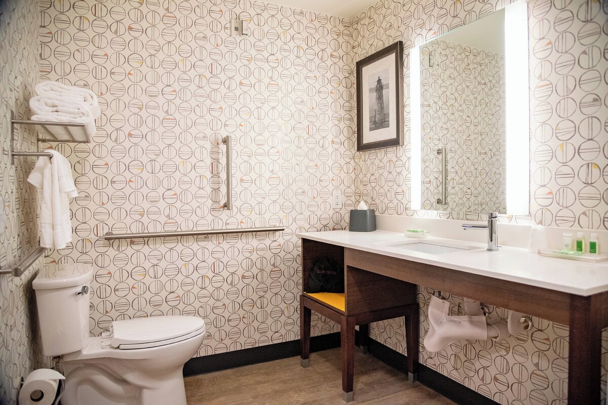 A bathroom with a patterned wallpaper, a toilet, a sink with a mirror, and a towel rack.