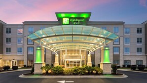 A Holiday Inn & Suites with a glass entrance canopy, multiple floors, and a landscaped entrance area. - Holiday Inn & Suites Savannah Airport - Pooler by IHG (Pooler)