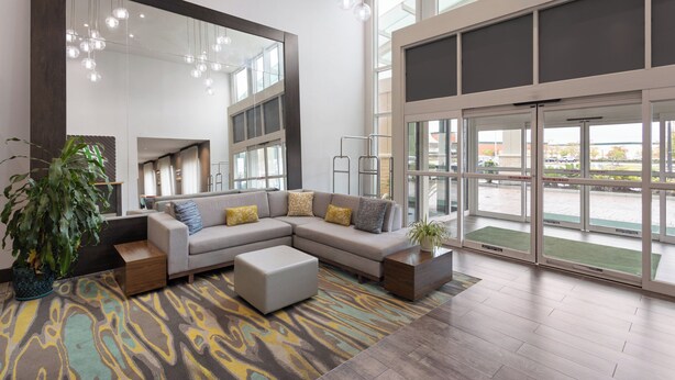 A modern hotel lobby with a large sectional sofa, a potted plant, and a patterned rug. - Holiday Inn & Suites Savannah Airport - Pooler by IHG (Pooler)
