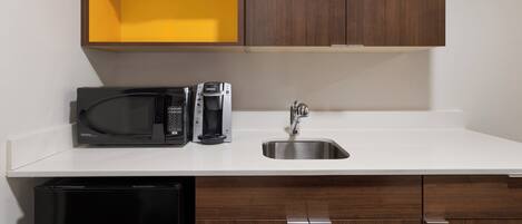 A compact kitchen with a microwave, coffee maker, and a sink.