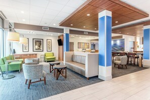 A hotel lobby with seating areas, a reception desk, and a dining area.