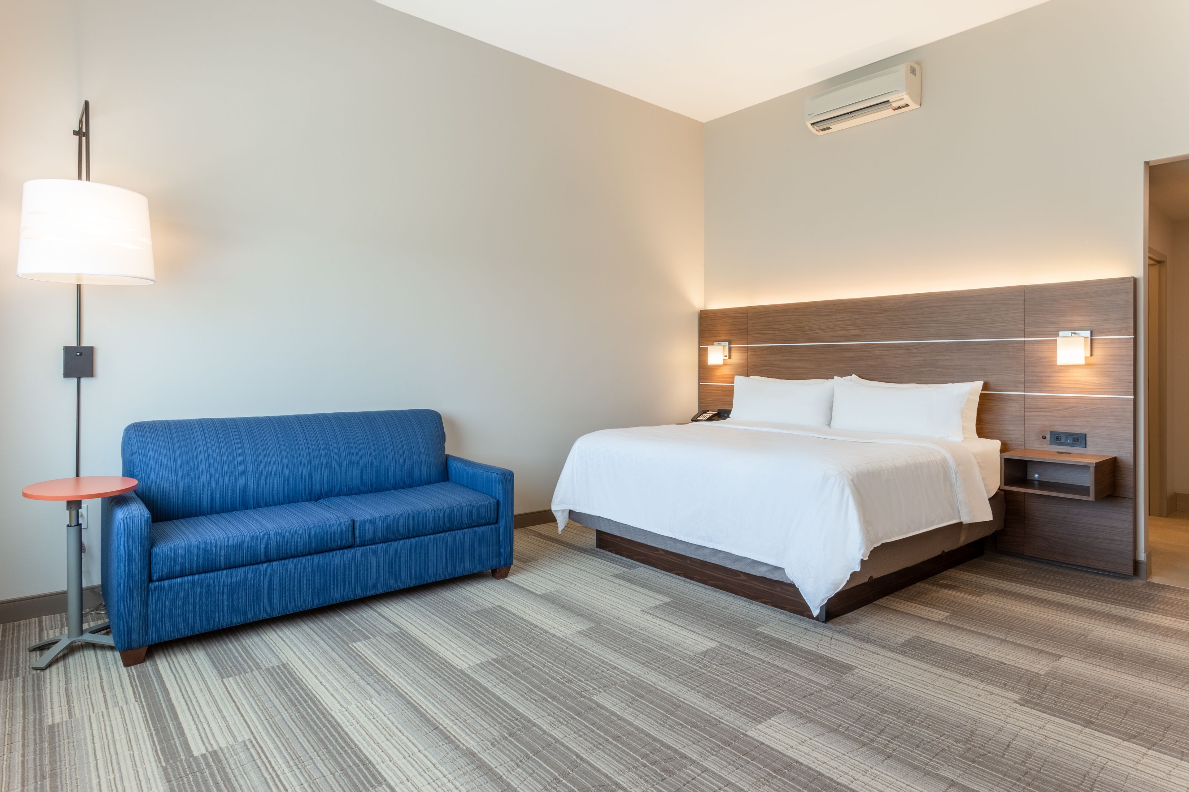 Una habitación de hotel con una cama, un sofá azul, una mesita y una lámpara de pared.