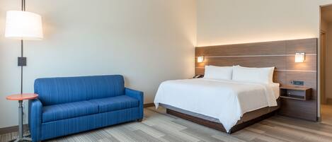 Una habitación de hotel con una cama, un sofá azul, una mesita y una lámpara de pared.