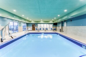 An indoor swimming pool with clear blue water, surrounded by blue-tiled walls and a ceiling with recessed lighting.