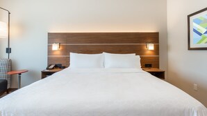 A hotel room with a large bed, wooden headboard, bedside tables with lamps, a telephone, and a chair. - Holiday Inn Express & Suites Springfield North by IHG (Springfield)