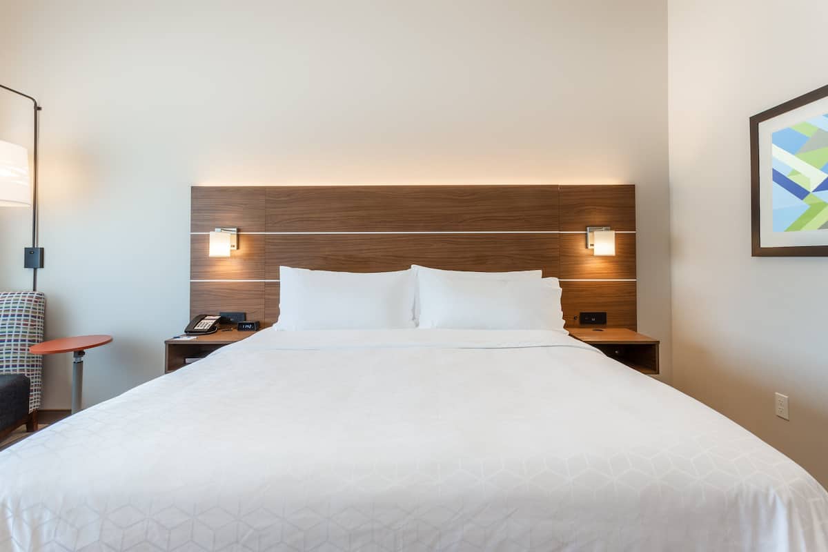 A hotel room with a large bed, wooden headboard, bedside tables with lamps, a telephone, and a chair.