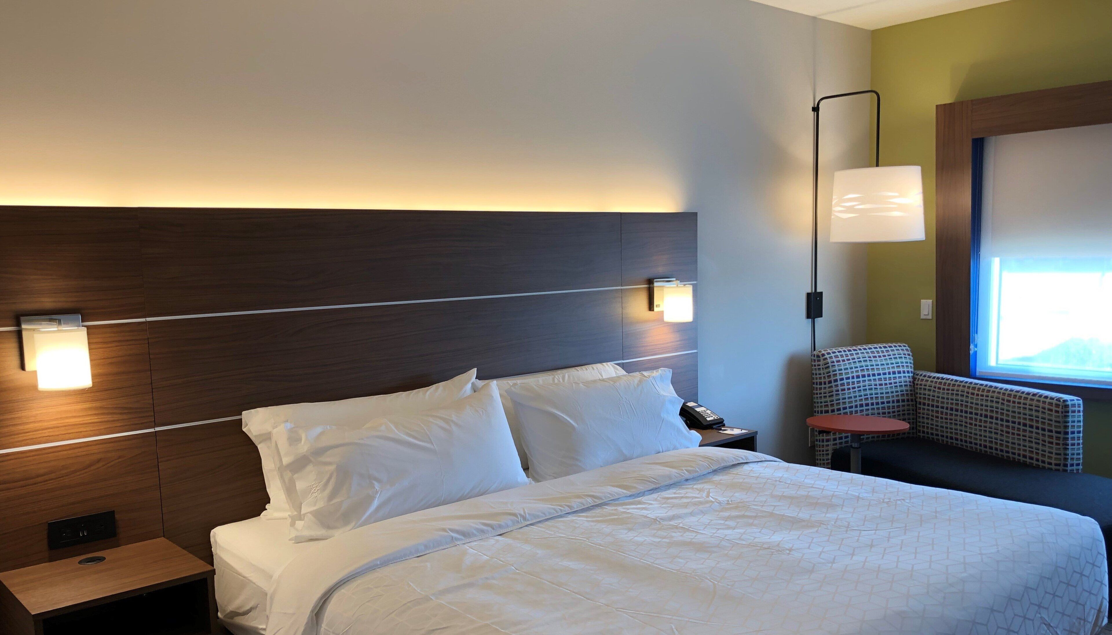 A hotel room with a large bed, bedside lamps, a small table, and a chair.