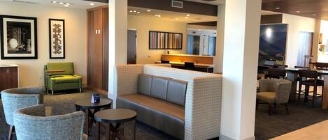 A hotel lobby with seating areas, a reception desk, and a kitchenette.