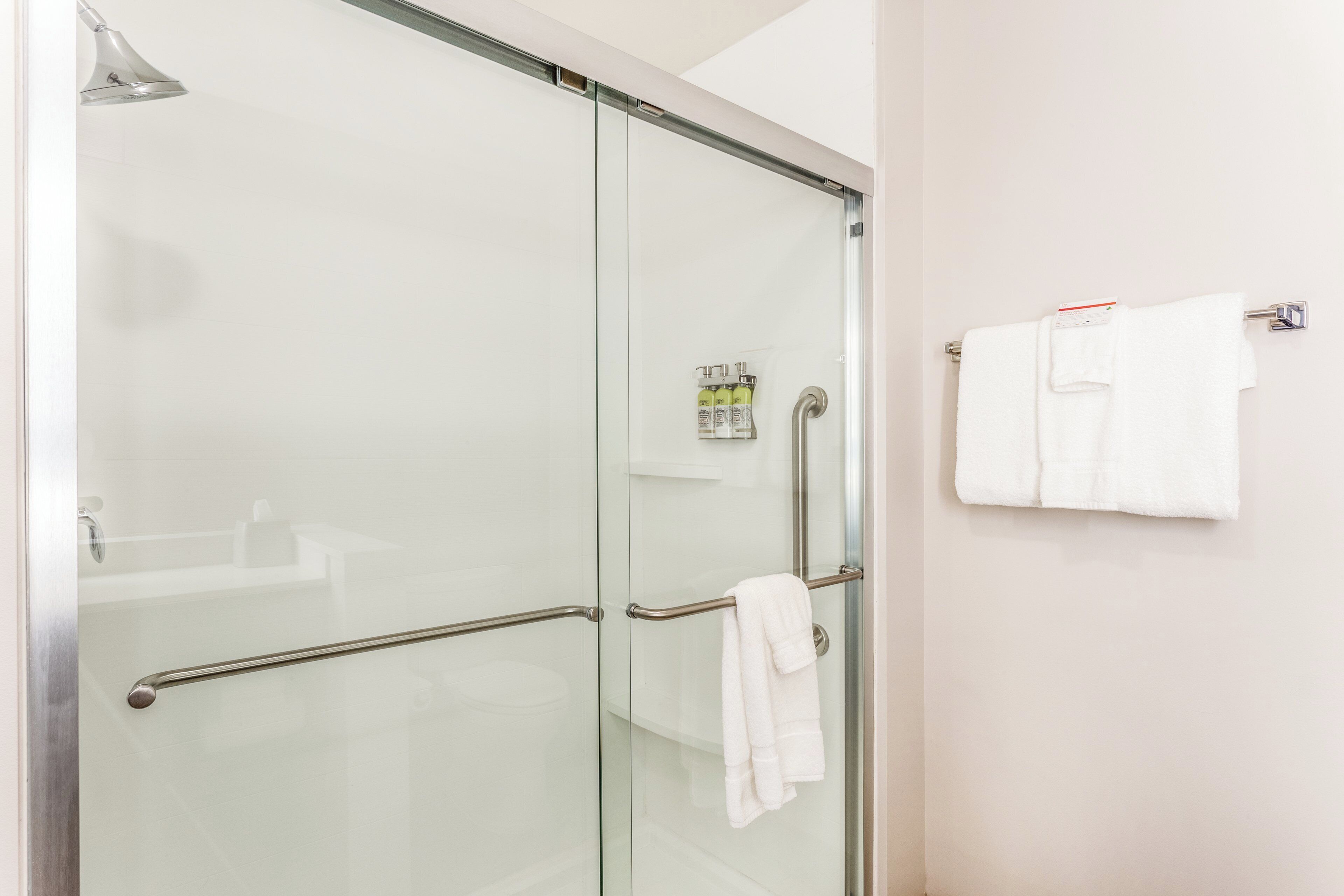 Un baño moderno con cabina de ducha de vidrio, un perchero con dos toallas y un dispensador de jabón en la pared.