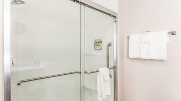 Un baño moderno con cabina de ducha de vidrio, un perchero con dos toallas y un dispensador de jabón en la pared.