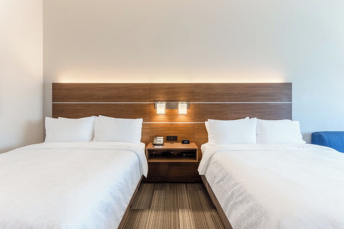 Een hotelkamer met twee bedden, een houten hoofdbord, nachtkastjes met lampen en een telefoon.