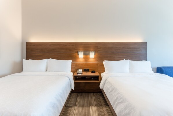 Een hotelkamer met twee bedden, een houten hoofdbord, nachtkastjes met lampen en een klein nachtkastje.