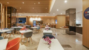 Un hall d’hôtel moderne comprenant différents espaces de détente, un comptoir d’accueil et une cuisine ouverte.